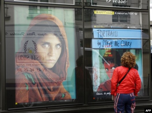 A woman in Paris looks at a  poster of the famous photograph of Sharbat Gula.
