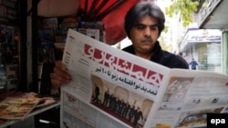 An Iranian man reads a copy of the 'Hamshahri' newspaper, featuring a picture of Iranian foreign minister Mohamad Javad Zarif and his counterparts from France, Germany, UK, China, Russia and the US, outside a kiosk in Tehran, 25 November 2014.