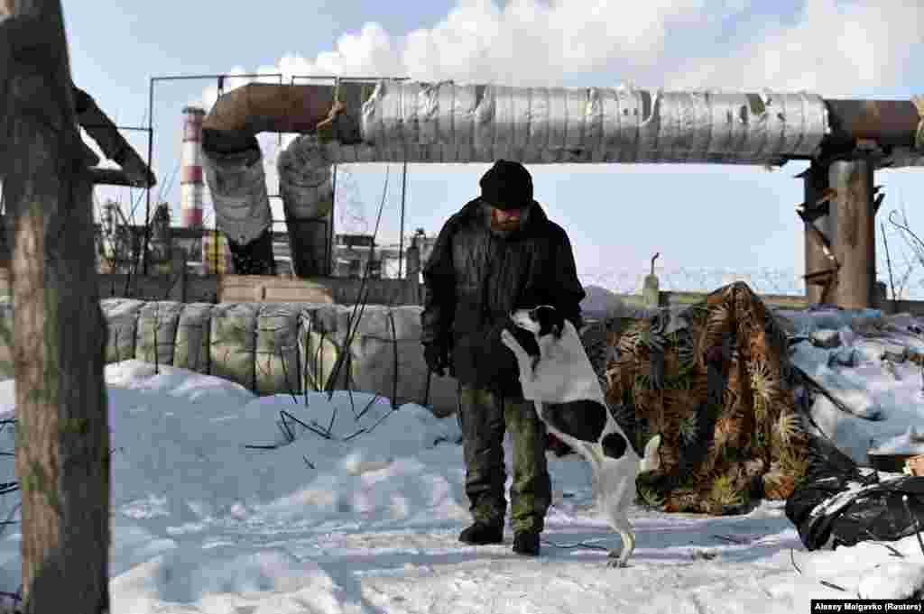 Aleksei Vergunov, 46, nicknamed &quot;Lyokha Boroda&quot; (Lyokha the Beard), stands near his makeshift shelter with his dog, Bella. He worries that -- in the haze of hard alcohol he drinks to keep warm and dull reality -- he might get severe burns by sleeping too close to the pipe. &nbsp;