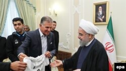 Iranian president Hassan Rohani (R) receives a jersey from Iranian national soccer team's Portuguese head coach Carlos Queiroz (L) during a reception at the presidential office in Tehran, June 14, 2017