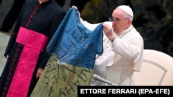 Папа Францішак паказвае сьцяг, прывезены яму з Бучы, падчас штотыднёвай агульнай аўдыенцыі. Ватыкан, 6 красавiка 2022