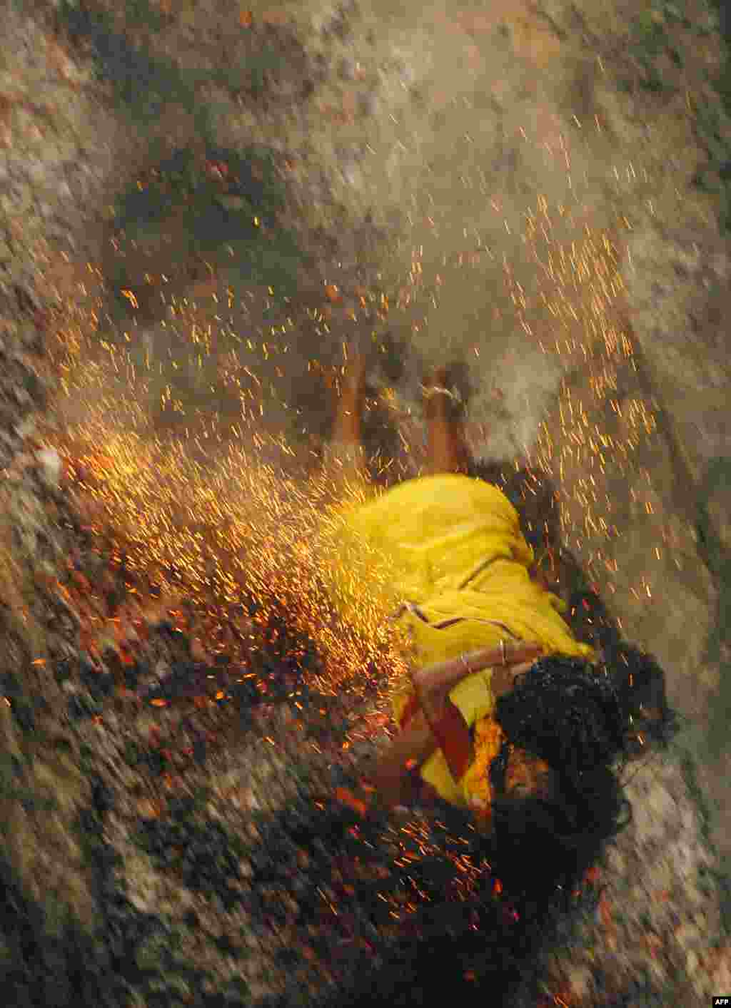 An Indian Hindu devotee falls on burning coals while holding her daughter during a coal run at the Maa Maariamma Mela in Jalandhar, India. The devotees run on fire after fasting for seven days to prove their devotion. The mother and daughter were both injured. (AFP/Shammi Mehra)