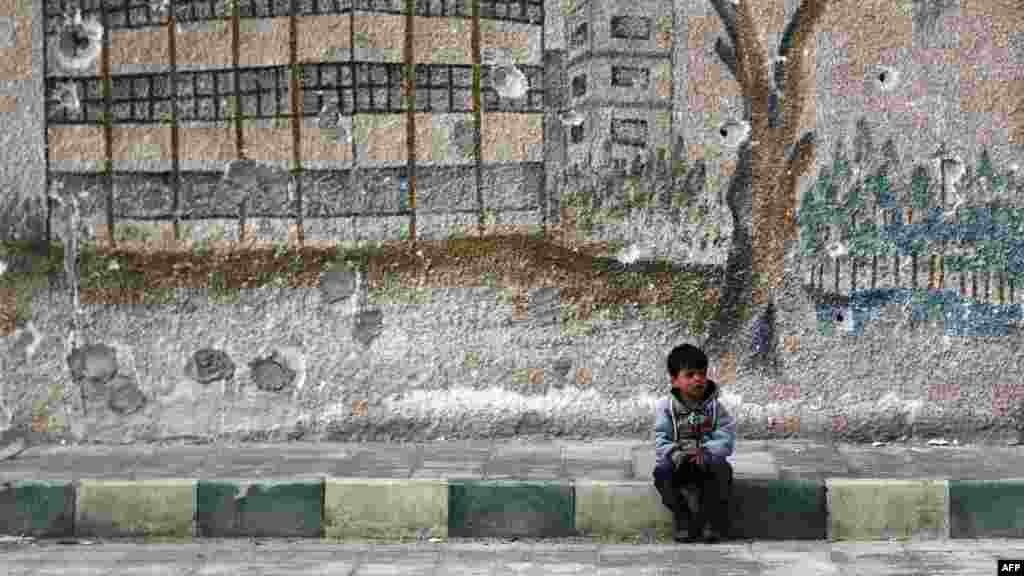 Gündogar Ghouta, Damaskyň etegi, ozalky mekdebiň okdan eleme-deşik bolan diwarynyň öňünde oturan çaga. (AFP/Abdulmonam Eassa)