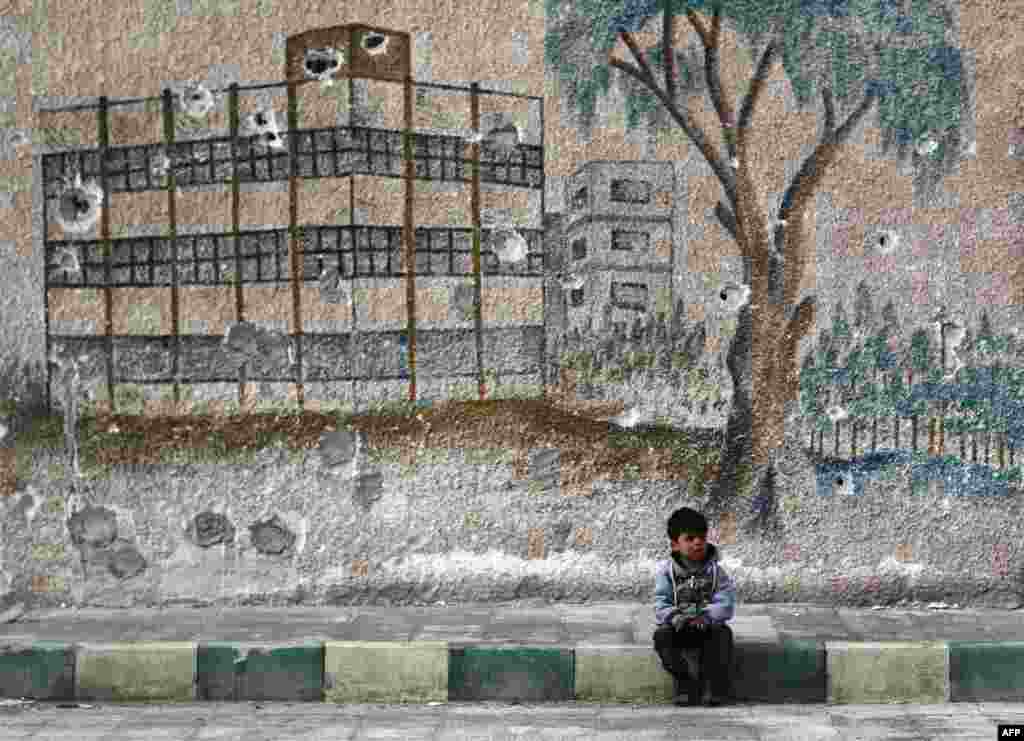 A Syrian child sits in front of a bullet-riddled mural on the wall of a former school in the rebel-held region of Eastern Ghouta, on the outskirts of the Syrian capital, Damascus. (AFP/Abdulmonam Eassa)