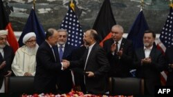 Afghan National Security Adviser Hanif Atmar (2R) and US Ambassador to Afghanistan James Cunningham (2L) hold their documents after signing a deal to allow some US troops to stay in Afghanistan in Kabul, September 30, 2014.