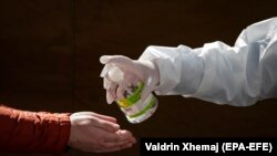 Një punëtor shëndetësor në Prishtinë dezinfekton duart e një qytetari. Prishtinë, prill 2020. 