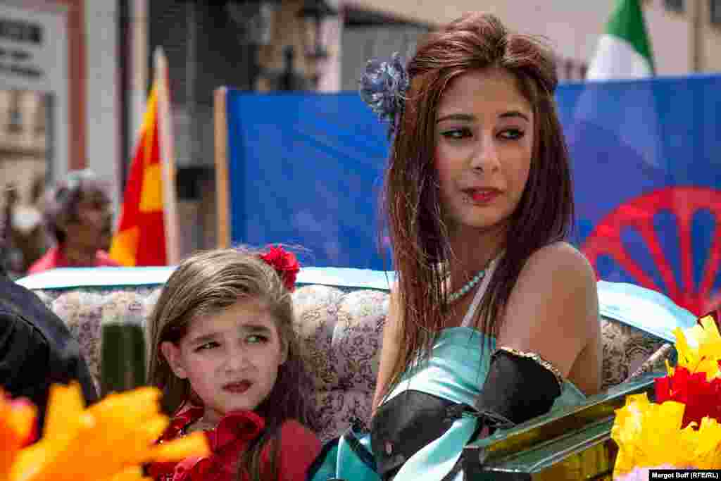 Girls ride in a horse-drawn carriage in front of the international Romany flag, which features a wagon wheel.