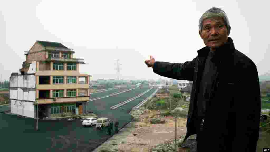 Luo Baogen points at his half-demolished apartment building, which stands in the middle of a newly built highway in China&#39;s eastern Zhejiang Province. Luo, 67, and his 65-year-old wife have waged a four-year battle to receive more than the $41,300 in compensation offered by the local government. Such a building is called a &quot;nail house&quot; in China, as such buildings stick out and are difficult to remove, like a stubborn nail. The road has yet to officially open, and state media carried conflicting accounts over whether Luo had finally agreed to accept an offer for his family&#39;s home. (AFP)
