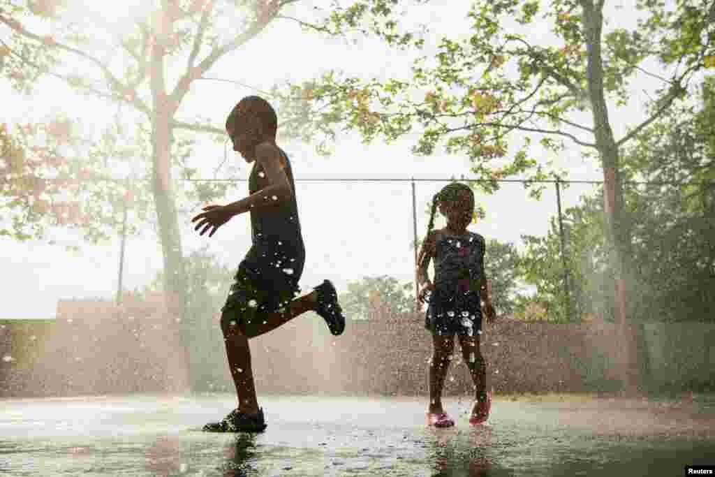 Children run through a sprinkler system installed inside a playground to cool off in the summer heat in New York City on July 17.