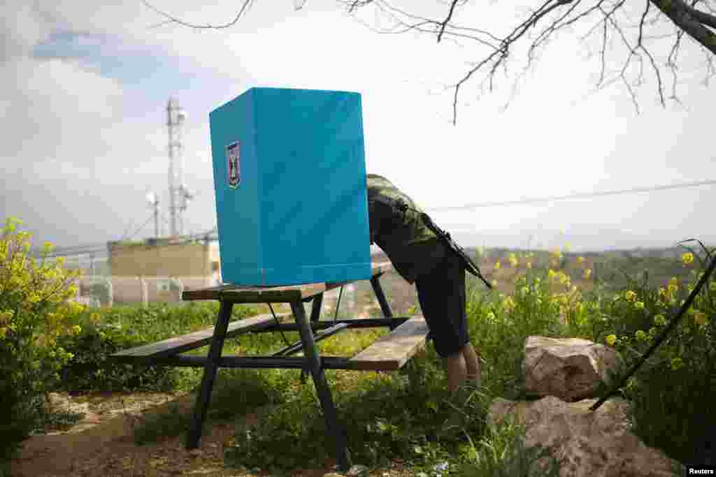 An Israeli soldier casts his ballot in parliamentary elections behind a mobile voting booth in the West Bank Jewish settlement of Migdalim, near Ariel. Millions of Israelis voted on March 17 in a tightly fought election, with Prime Minister Benjamin Netanyahu facing an uphill battle to defeat a strong campaign by the center-left opposition to deny him a fourth term in office. (Reuters/Amir Cohen)