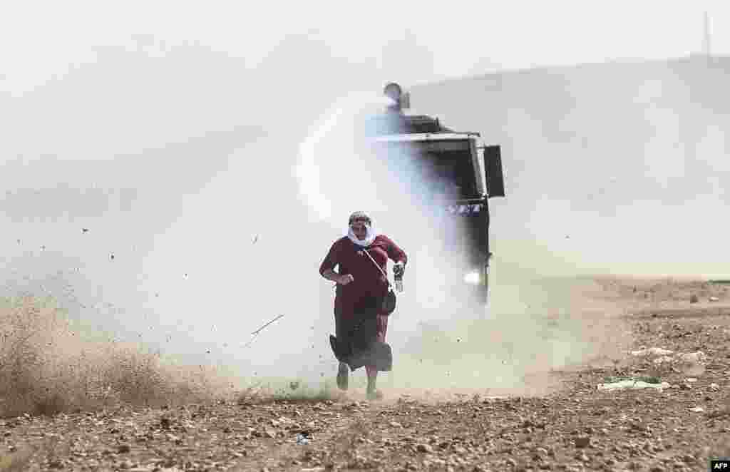 A Kurdish woman runs away from a water cannon near the Syrian border after Turkish authorities temporarily closed the border at the southeastern town of Suruc in Sanliurfa Province. Turkey said on September 22 that some 130,000 people had flooded across its border from Syria as Kurdish fighters battled Islamic State militants trying to capture a strategic town. (AFP/Bulent Kilic) 