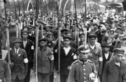 Polish volunteers stand armed with scythes.