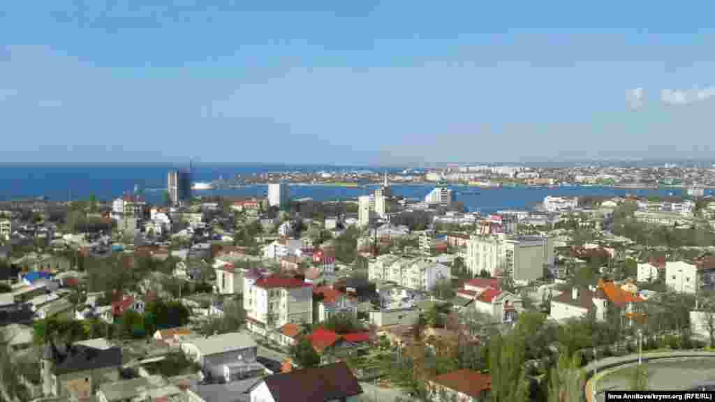 Панорама весняного Севастополя. Цей вид мало змінився через три роки. Але є одна особливість – будівля, якої не стало з приходом в місто російської влади. Знесення сірої недобудованої шістнадцятиповерхівки (в лівій частині кадру) севастопольці запам'ятали надовго. Для вибухових робіт були запрошені російські фахівці. Впоралися не відразу: прогримів перший вибух, і будівля нахилилася, прогримів другий – частина будинку встояла, решта розбирали вручну. Новоутворене звалище на місці колишнього будмайданчика довго красувалося в центрі міста, поруч з історичним пам'ятником. Причина знесення – порушення містобудівних норм. Будівлю не можна, звалище можна Севастополь, 17 квітня 2014 року, площа Повсталих
