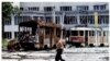 A Bosnian teenager carries containers of water in front of destroyed trams at Skenderia Square in Sarajevo on June 22, 1993. A woman passes through the same square on April 4, 2012.