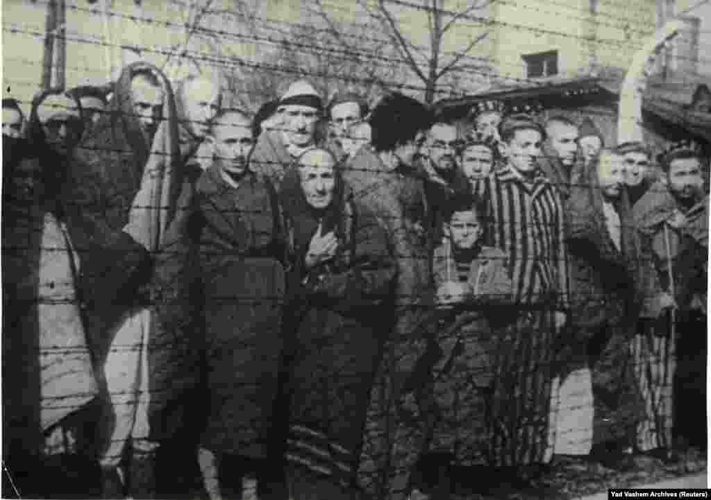 Sovjetske jedinice Crvene armije su 27. januara 1945. godine, na juriš i uz znatne gubitke, oslobodile Auschwitz, najveći nacistički koncentracijski logor u Drugom svjetskom ratu. na fotografiji: preživjeli holokausta stoje iza ograde od bodljikave žice nakon oslobađanja Auschwitz-Birkenaua 1945. godine.