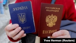 Женщина держит украинский и российский паспорта у офиса Федеральной миграционной службы России, открытого в Симферополе после аннексии Крыма, 7 апреля 2014 года. Архивное фото