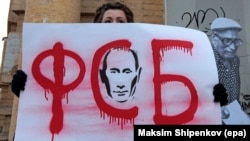 A demonstrator in Moscow holds up a sign saying "FSB" with a portrait of Vladimir Putin demanding freedom for political prisoners. The FSB is "closed in on itself and accounts to no one. In that sense, the FSB now is more frightening and more powerful than the KGB was," an NGO lawyer says.