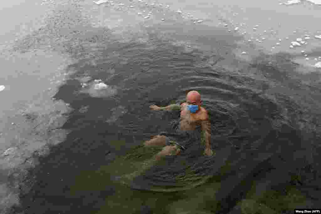 A man wearing a protective face mask swims in a partly frozen lake as snow falls in Beijing, China. (AFP/Wang Zhao)&nbsp;