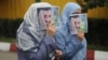 Two women cover their faces with images of Mahmud Ahmadinejad. (file photo)