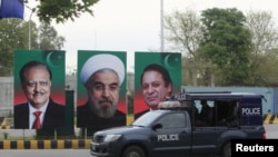 A Pakistani police vehicle patrols near the portraits of the Pakistani and Iranian leaders displayed along a road during Rohani's visit.