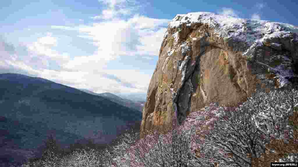 На фоне густо укрытого снегом леса возвышается остроконечная скала. Это Кок-Таш, что в переводе с крымскотатарского &laquo;синий камень&raquo;, одна из вершин внутренней гряды Крымских гор