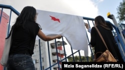 Protesters display a bed sheet with a red stain in the shape of Georgia at the protest outside the National Forensics Bureau.