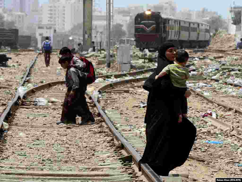 People cross rail tracks as a train arrives in Karachi, Pakistan. Every year, hundreds of people are killed or injured after being hit by trains in Pakistan. (EPA-EFE/Rehan Khan)