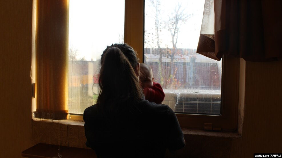 Девочка-подросток со своим ребенком смотрит в окно. Шымкент. 