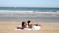 Женщины в масках загорают на пляже после ослабления карантинных мер в некоторых регионах Испании. Валенсия, 18 мая 2020 года.