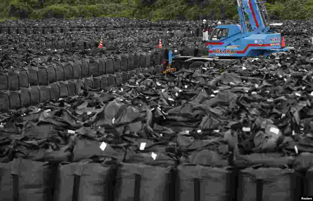 Workers move bags of waste containing soil, leaves, and debris to a storage site in Naraha. The Japanese government is seeking a site for permanent storage of radioactive refuse.