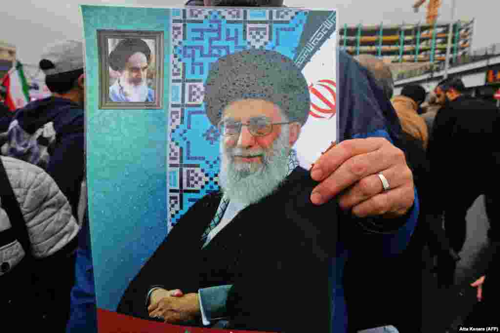An Iranian holds a poster showing Supreme Leader Ayatollah Ali Khamenei with a small portrait in the corner showing Islamic Revolution founder Ayatollah Ruhollah Khomeini.