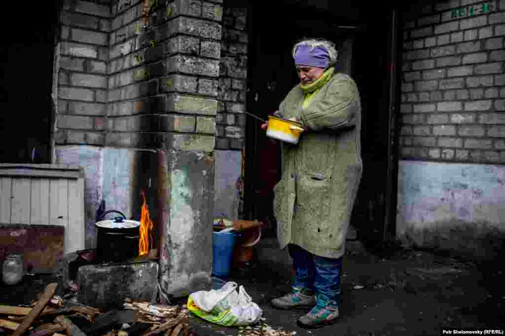 A woman cooks over an open fire. Electricity, gas, and water supplies have been cut off.