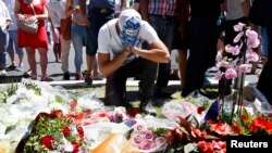 A man reacts near bouquets of flowers as people pay tribute near the scene where a truck ran into a crowd at high speed killing scores and injuring more who were celebrating the Bastille Day national holiday, in Nice, France, July 15, 2016. 