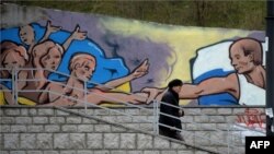 A woman in Simferopol walks past a mural depicting Russian president Vladimir Putin giving a hand to Ukranians. 