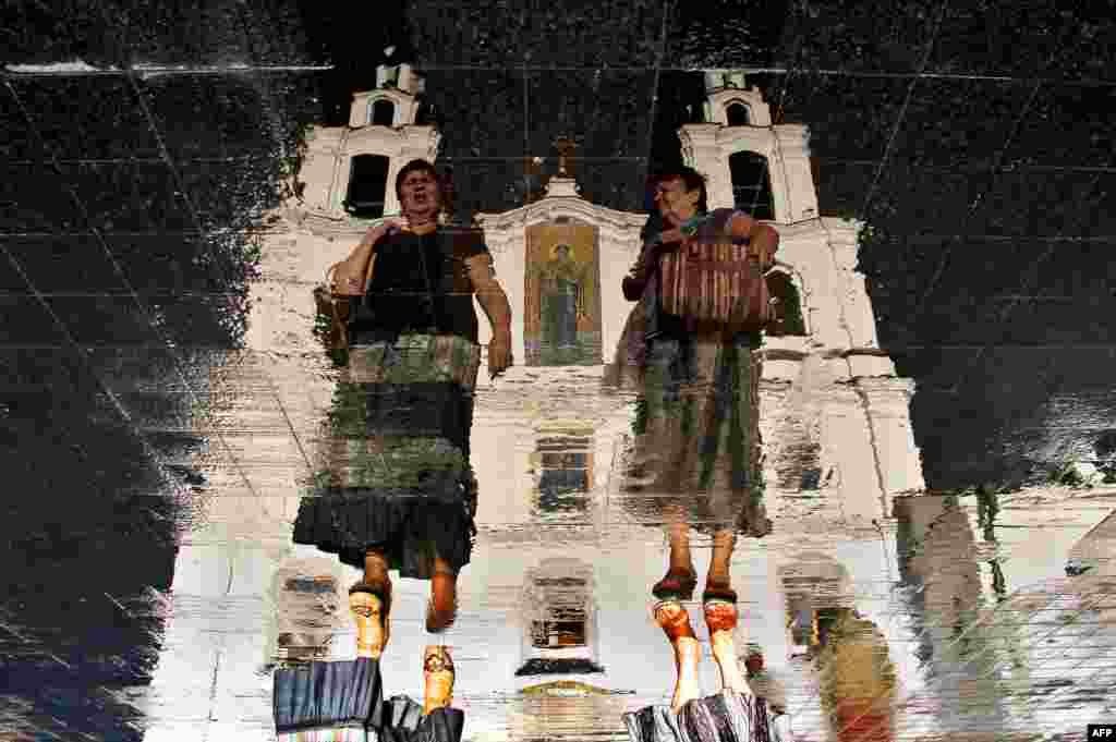 Two women walk in front of the Holy Spirit Orthodox cathedral as they are reflected in the wet tablets of a roadway in the Belarusian capital, Minsk. (AFP/Sergei Gapon)