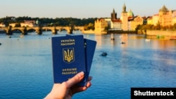 Generic – Woman's hand holding two Ukrainian passports in front of Prague old town cityscape