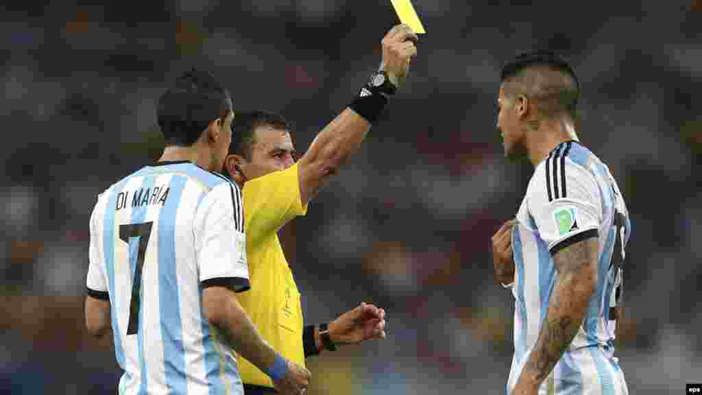 Сальвадорский рефери Хоель Агилар (в сентре) показывает желтую карточку аргентинскому футболисту Маркусу Рохо (справа) во время матча со сборной Боснии и Герцеговины.