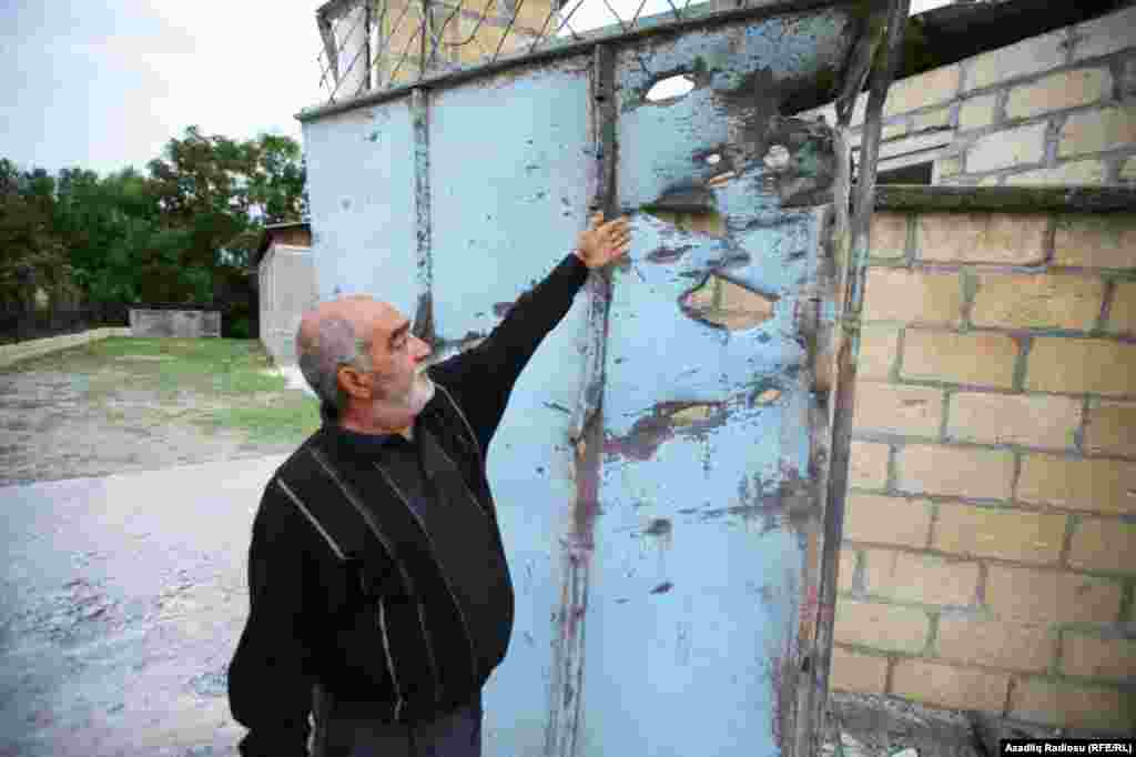 В городе Тартар (Азербайджан) мужчина показывает дыры в поврежденных от обстрелов воротах дома