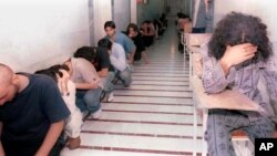 While covering their faces, Iranian youth who had been arrested in recent student protests, sit in a hallway of the Evin prison, in Tehran, Iran, Sunday, June 15, 2003. (AP Photo)