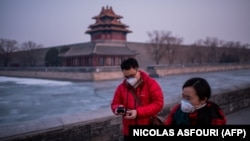 A couple wearing protective masks to prevent the spread of the coronavirus walk near the Forbidden City in Beijing.