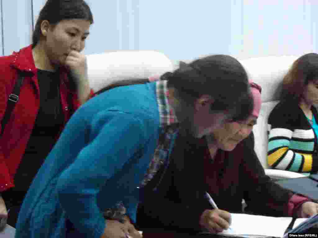 Две девушки и их мать изучают объявления на ярмарке вакансий в Шымкенте.