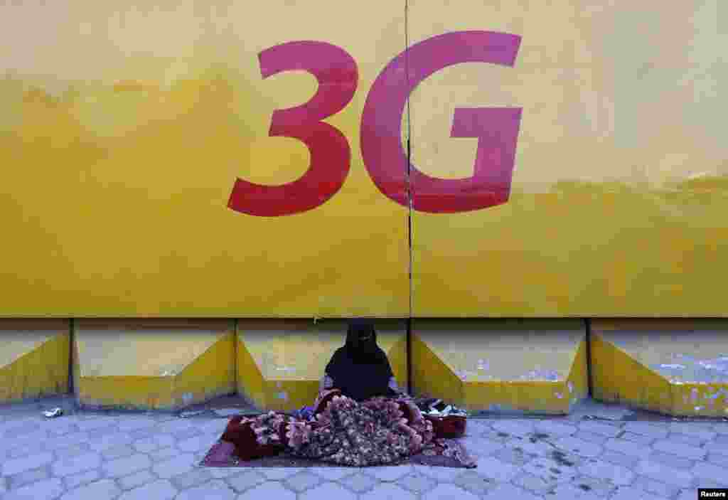 An Afghan woman begs under a 3G logo in Kabul on March 8 (International Women&#39;s Day)