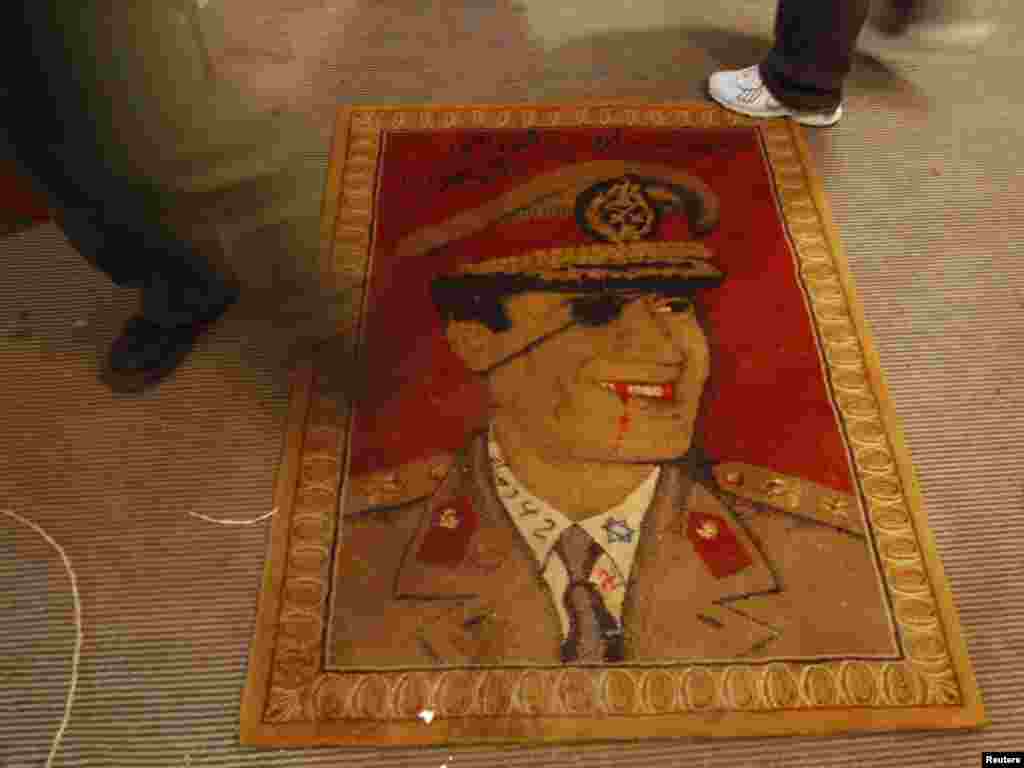 A protester walks over a rug depicting a defaced portrait of Libyan leader Muammar Qaddafi in Benghazi. Photo by Suhaib Salem for Reuters
