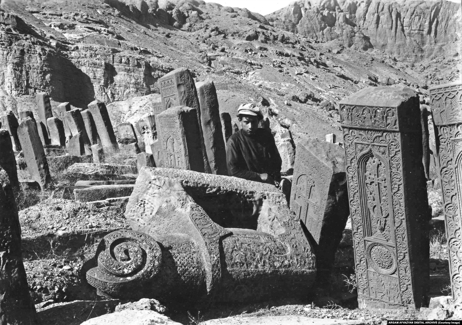 A young man poses among khachkars and a stone ram in the Julfa cemetery in 1915.