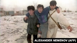 Двое чеченских бойцов несут раненного в результате обстрела на окраине Грозного 25 декабря 1994 года, когда российские вооруженные силы усилили бомбардировку города