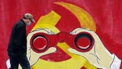 مردی با ماسک در کنار نقاشی نشان حزب کمونیست چین