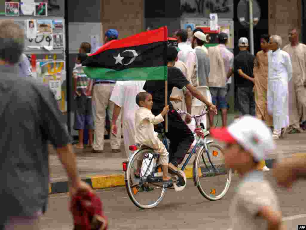 A young boy riding on the back of a bicycle holds his national flag in Tripoli on September 9. (Photo by AFP)