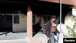 FILE: An Afghan policeman walks at the government district building after a Taliban attack in Khawaja Omari district of Ghazni province in April.