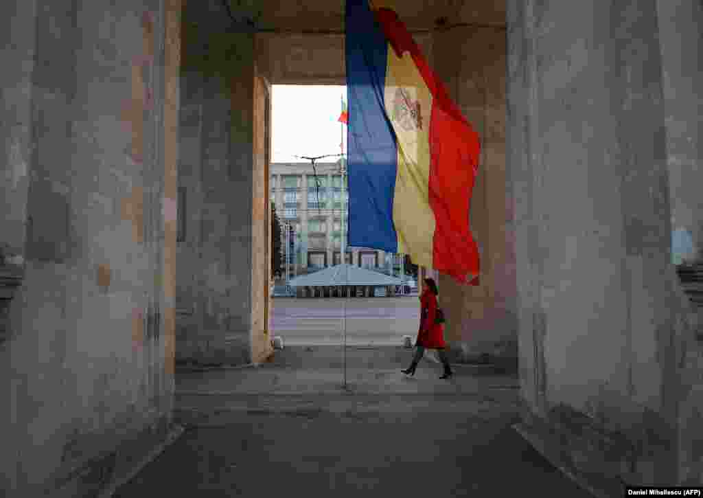 A woman walks under the Triumphal Arch next to the Moldovan flag in Chisinau.