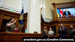 Președintele Ucrainei Volodimir Zelenski aplaudă anunțul făcut de Boris Johnson în Parlamentul ucrainean pe 3 mai 2022.